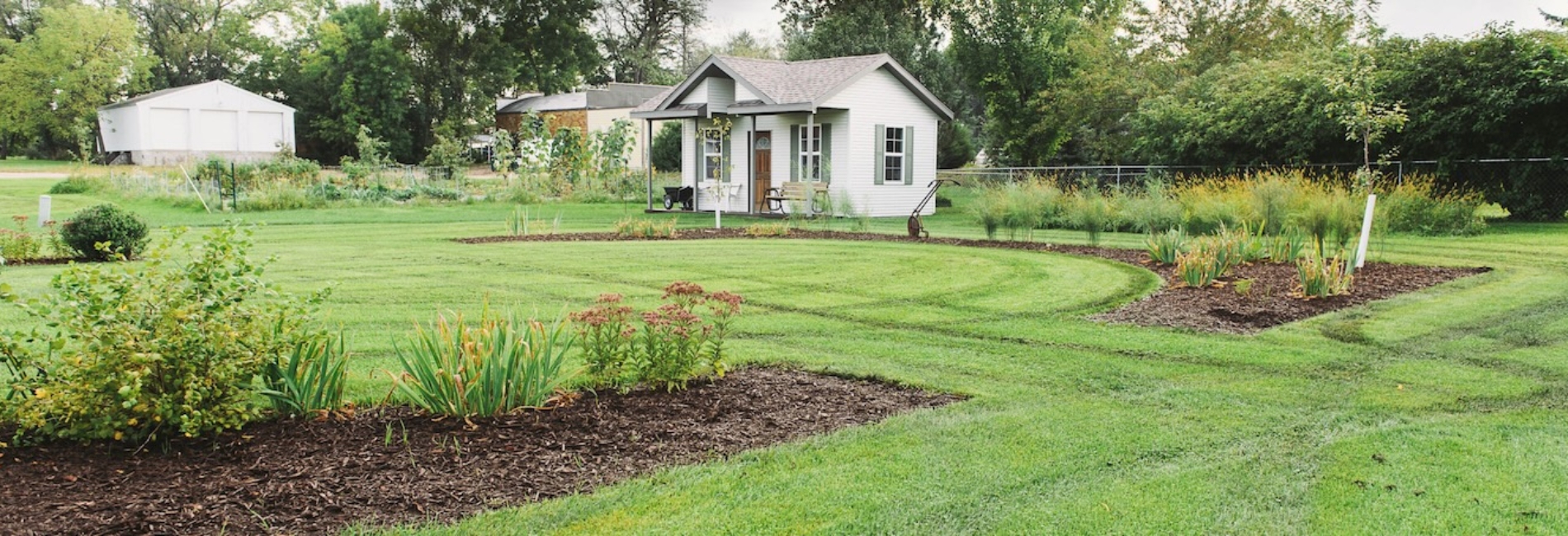 small white house with a bench our front with mowed green lawn and flower sections
